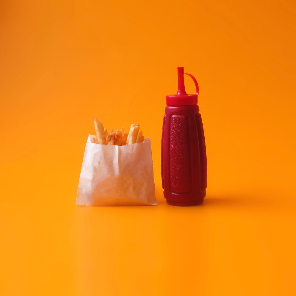 Um pacote de batata frita ao lado de um pote de ketchup em um fundo amarelo.