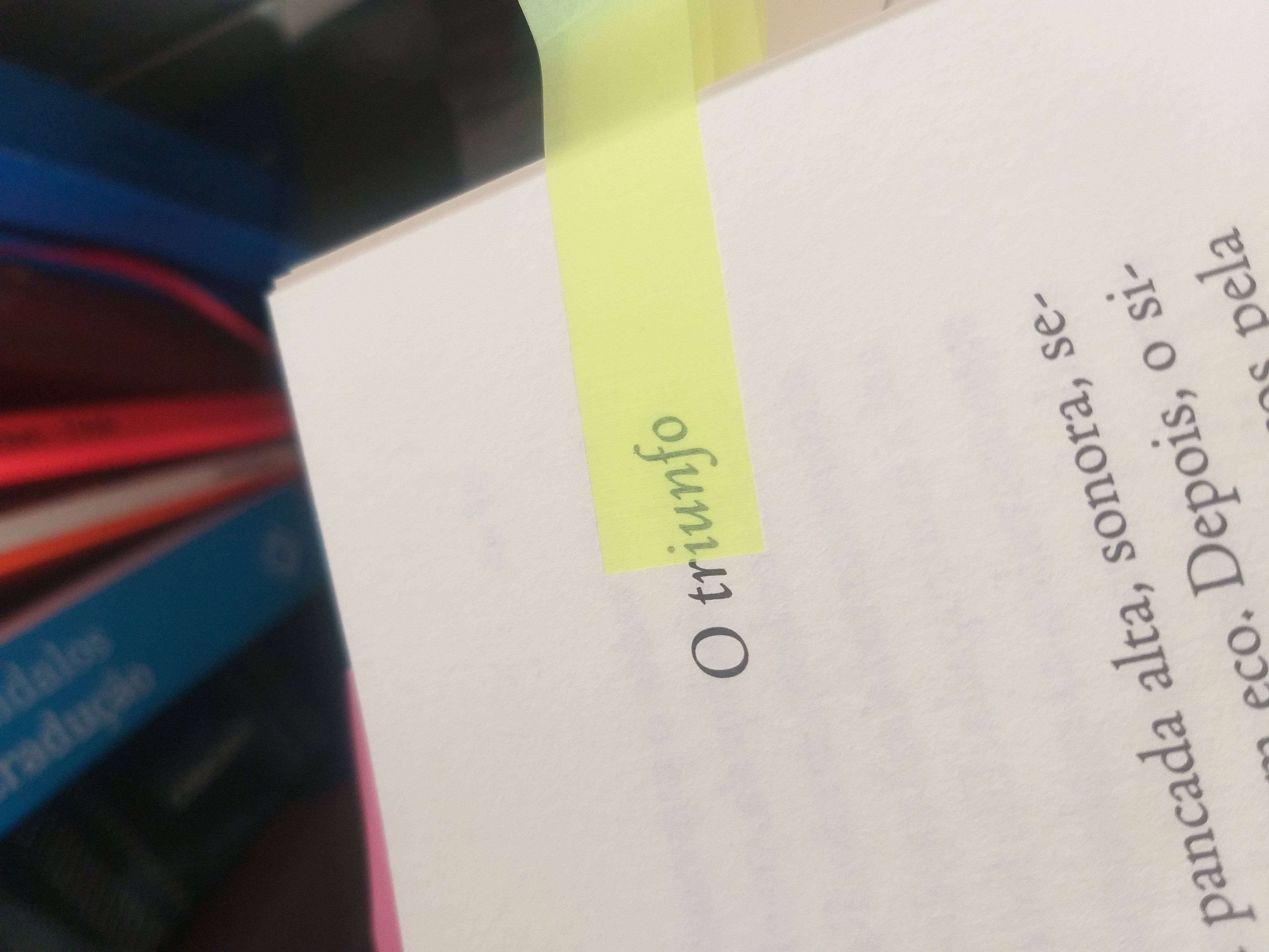 página de um livro com o título "O triunfo" e um post-it amarelo sobre as letras do título.